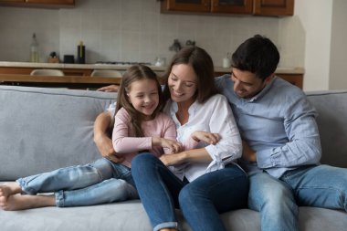 Mutlu ebeveynler, anne ve baba kucaklaşıyor, gıdıklıyor küçük kız çocuğu, rahat koltukta oturuyor, eğleniyor, eğleniyor, aile eğlencesi, ebeveynlik, gülüyor.