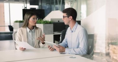 Tablet kullanan iki genç Avrupalı takım arkadaşı, modern çalışma alanında oturan gözden geçirme kağıtları, vizyon ve görüşleri paylaşmak, yeni ticari anlaşma ayrıntılarını gözden geçirmek, ortak proje üzerinde çalışmak. Takım çalışması, resmi toplantı.