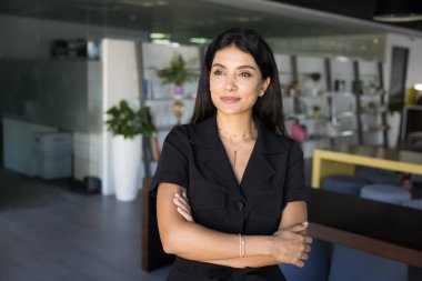 Ofiste çalışan, kollarını kavuşturmuş, yaratıcı fikirleri düşünen, yeni iş projeleri planlayan dalgın, kendine güvenen Ortadoğulu profesyonel bir kadın. Sıradan kadın portresi.