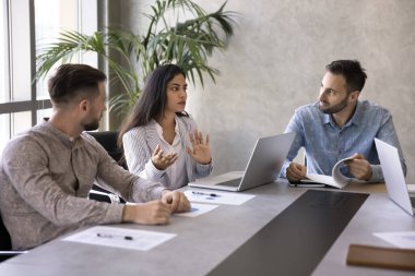 Ciddi genç Hintli iş kadını beyin fırtınası toplantısında iş arkadaşlarıyla ve erkek patronla konuşuyor. Çalışma projesi stratejisini, yaratıcı fikirleri tartışan çeşitli iş arkadaşları.