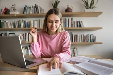 Bilgisayarda bir yığın ders kitabı okuyan, bireysel işler için halk kütüphanesini ziyaret eden, makale yazan, makale yazan, araştırma yapan, kitap sayfasına işaret eden,