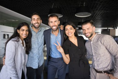 Mutlu çoklu etnik çeşitlilikteki şirket arkadaşları birbirlerine yakın durup, sarılırlar, kameraya bakarlar, gülümserler, gülerler, zafer işareti yaparlar. Başarılı iş arkadaşları portresi