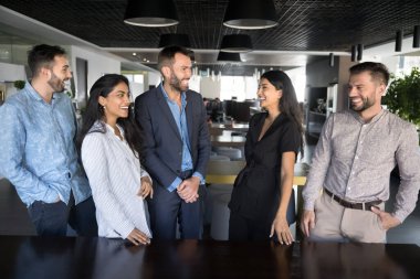 Başarılı takım çalışmalarından keyif alan neşeli iş arkadaşları, çalışma alanında bir arada duruyorlar, konuşuyorlar, gülüyorlar, şirket başarılarını tartışıyorlar, takım başarılarını tartışıyorlar.