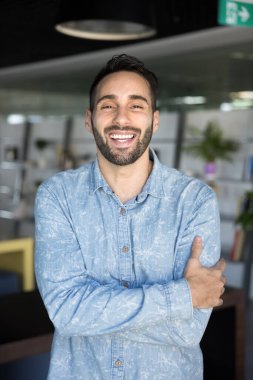 Neşeli, pozitif, yakışıklı İspanyol girişimci kameraya bakıyor ve gülüyor, kolları bağlı, gülümsüyor. Mutlu çekici iş adamı, sıradan, dikey vesikalık portresiyle.