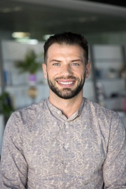 Mutlu çekici genç iş adamı, proje yöneticisi, müteahhit, şirket lideri dikey portre başı. Sıradan gömlekli yakışıklı adam dişlek gülüşlü kameraya bakıyor.