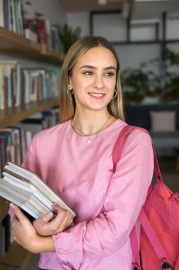 Bir yığın ders kitabı tutan mutlu genç kız halk kütüphanesinde kitaplıkların önünde duruyor, başka tarafa bakıyor, gülümsüyor. Kitapçıdaki raflarda kitap taşıyan bir kadın müşteri. Dikey çekim