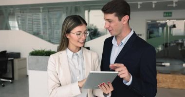 Profesyonel işbirliği, iş toplantısı, iş yerinde teknoloji. Dijital tablet kullanan iki genç takım arkadaşı, çevrimiçi görev veya proje üzerinde çalışıyorlar, satış sonuçlarını izliyorlar, borsa verileri