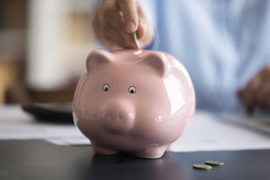 Kırpılmış kadın eli, pembe kumbaraya bozuk para koyuyor. Gelecek için para biriktirmek, sağlık sigortası, planlama yatırımı, aile bütçesi yönetimi, muhasebe kavramı