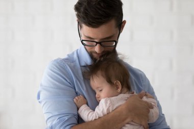 Huzurlu, gözlüklü genç bir baba kucağında uykulu bir kız çocuğu, sallanan, sakinleştiren bir çocuk, ebeveynliğin, babalığın, çocuk bakımının, evde boş vakit geçirmenin keyfini çıkarıyor. Baba olma konsepti