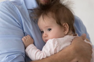 Babasının kollarında kıvırcık saçlı tatlı bir bebek, başka tarafa bakıyor. Yeni baba kucağında küçük bir kız çocuğu, sakinleştirici, sallanan bir çocuk, sevgiyle sarılıyor, özen gösteriyor. Babalık, çocuk bakımı kavramı. Kapat.