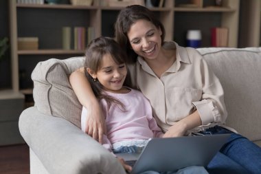 Pozitif anne ve neşeli sevimli kız evdeki kanepede oturup dizüstü bilgisayarda komik bir film izliyor, aile eğlencesi, eğlence, internet bağlantısı teknolojisinin tadını çıkarıyor.