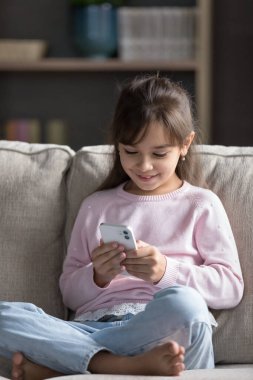 Neşeli anaokulu tatlı kızı akıllı telefonu evde tek başına kullanıyor, daktilo çekiyor, mesaj yazıyor, ekrana bakıyor, gülümsüyor. Cep telefonuyla öğrenme uygulaması yapan sevimli bir anaokulu çocuğu.