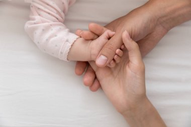 Yeni anne küçük bebek avucuna dokunuyor. Anne, beyaz giysi giyen bir çocuğun sevimli elini tutuyor. Yaklaş, kırpılmış atış. Annelik, doğum kavramı