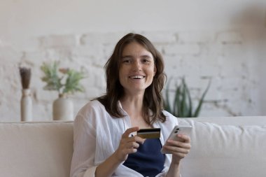 Mutlu mutlu bin yıllık kredi kartı kullanıcısı kız portresi. Neşeli genç kadın, banka müşterisi akıllı telefondaki sanal ödeme uygulamasını kullanıyor, kameraya bakıyor, gülümsüyor.