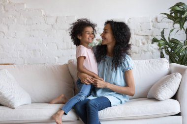 Mutlu Milenyum Siyahi Anne kucağında sevimli, neşeli küçük bir kız çocuğu, kucağında kanepe, kucağında sevgi, ilgi, şükran, çocukla konuşma, gülüşmeler. Annelik, aile kavramı