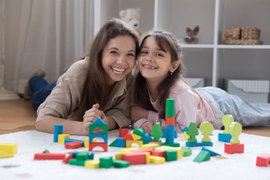 Neşeli genç bir anne ve sevimli pozitif bir kız çocuğu sıcak zeminde renkli inşaat bloklarında dinleniyor, gülüyor, kameraya bakıyor. Anne ve anaokulu çocuğu birlikte oynuyorlar. Ev resmi