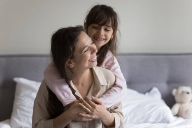 Heyecanlı bir anne ve kız çocuğu aşk, şefkat ve ev yatağında oynaşıp sarılıyorlar. Anne küçük tatlı çocuğu sırtında taşıyor, gülüyor, eğleniyor, oyun oynuyor.