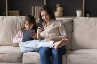 Pozitif anne ve ciddi çocuk evdeki koltuğa yakın oturan cihazlara odaklandılar, cep telefonu kullanıyorlar, online iletişim için tablet kullanıyorlar, sohbet ediyorlar, çalışıyorlar, internette sanal oyun oynuyorlar.