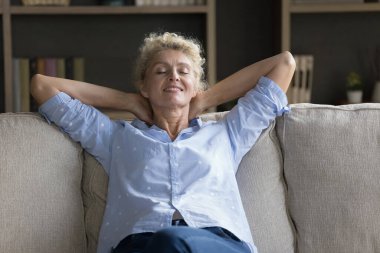 Positive calm mature senior woman resting on couch with closed eyes, relaxing, stretching body, leaning on back with open arms, enjoying silent break, leisure at home, meditating breathing fresh air clipart