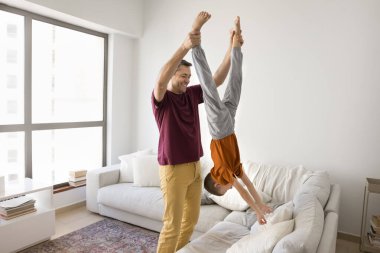 Neşeli, şefkatli güçlü İspanyol baba çocuğu baş aşağı kaldırıyor, oğlanların bacaklarını tutuyor. Oyuncu aktif baba küçük çocukla oynuyor, oğlunu eğlendiriyor, evde eğlenceli aile eğlencelerinin tadını çıkarıyor.