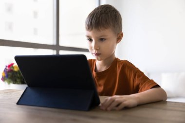 İlk okul çağındaki çocuk tablet bilgisayarında online öğrenim görüyor, eğitim amaçlı internet servisini ev masasında dijital aletler üzerinde kullanıyor, video, film izliyor, oyun oynuyor.