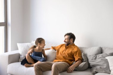 Küçük tatlı bir kız çocuğu ve orta yaşlı mutlu bir Latin baba evde kanepede dinleniyor, konuşuyor, gülüyor, sohbet ediyor, birlikte eğleniyor, aile eğlencesi, babalık, çocukluk.