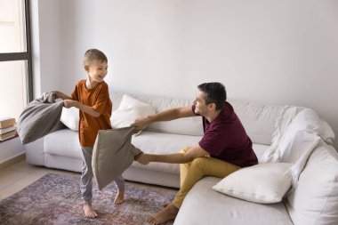 Neşeli bir Latin baba ve heyecanlı, aktif bir çocuk. Evde yastık savaşı oynuyorlar. Yastık sallıyorlar, birbirlerini beyaz koltukta dövüyorlar.