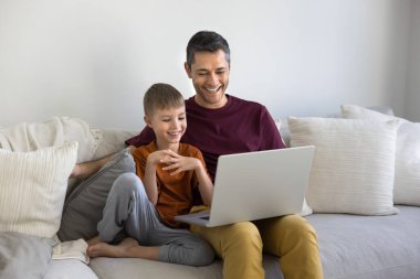 Mutlu İspanyol baba ve neşeli çocuk film, dizi, dizüstü bilgisayar izliyor, gülümsüyor, gülüyor, çevrimiçi servis kullanıyor, alışveriş, rezervasyon, internet siteleri...