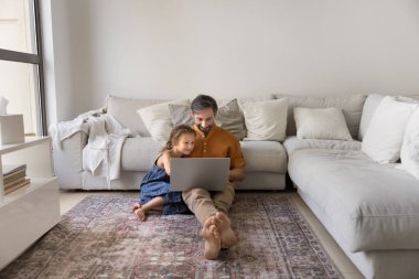 Pozitif baba ve küçük kız evde oturma odasındaki halı döşeli ısıtma katında birlikte dinleniyorlar, kanepede oturuyorlar, dizüstü bilgisayar kullanıyorlar, film izliyorlar, dizi izliyorlar. Geniş gövde gösterisi