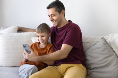 Mutlu 40 'lı yılların İspanyol babası cep telefonundan küçük oğluna internet içeriği gösteriyor. Positif baba ve sevimli çocuk birlikte cep telefonu kullanıyor, evde internet teknolojisinden keyif alıyorlar.