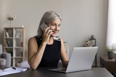 Evden uzakta bağımsız olarak çalışan yaşlı bir kadın bilgisayardaki cep telefonu kontrol verileri ile çevrimiçi konuşuyor. Uzaktan İşçi Yöneticisi Danışmanı Telefon görüşmesi yapmak ya da ekomünikasyon emrini doğrulamak