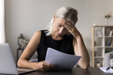 Kafası karışmış, yaşlı, serbest çalışan girişimci kadın finansal borç olasılığını düşünüyor. İflasın para kaybetmesi ihtimali. Endişeli kıdemli bayan serbest çalışan resmi gazetede kötü haberler aldı.