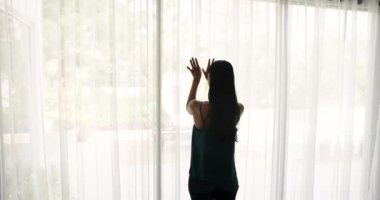 Dikiz aynasındaki genç kadın panoramik pencerenin yanında duruyor, perdeleri açıyor, teras manzarasına şezlonglar ve yeşilliklerle hayran kalıyor, yeni günü kutlamak tatilde mutlu hissettiriyor. Seyahat, tatil, yeni hayat.