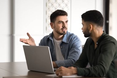 Kendine güvenen genç Orta Doğulu başlangıç lideri laptop 'da iş ortağıyla konuşuyor, proje pazarlama görevini anlatıyor, konuşuyor, ofis masasında takım çalışması için iş arkadaşlarıyla görüşüyor.