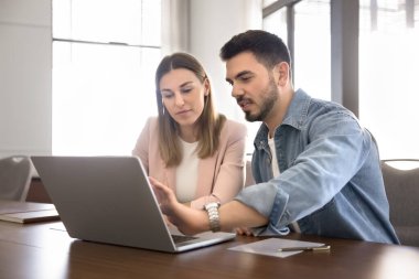 İki meşgul genç çalışan dizüstü bilgisayarla konuşuyor, ekrana işaret ediyor, birlikte online girişim projesi üzerinde çalışıyorlar, internette sunum izliyorlar, iş görevlerini tartışıyorlar, ağ kuruyorlar.