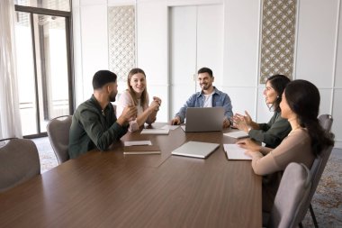 Olumlu genç iş arkadaşları takım çalışması, işbirliği, yaratıcı proje üzerine beyin fırtınası, işbirliği odasında konuşma, fikirler, pazarlama stratejisi için büyük masada buluşuyorlar.