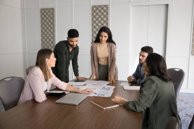 İstatistik kağıtları üzerinde birlikte çalışan, pazarlama raporlarını analiz eden, oturan, büyük masada duran, konuşan, belgeleri kontrol eden çok ırklı iş ortaklarından oluşan bir ekip.