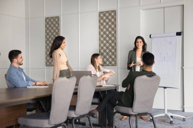 Kendine güvenen genç Latin iş eğitmeni kadın proje istatistiksel verilerini çeşitli yönetici takımlarına sunuyor, beyaz tahtada konuşuyor, mali tabloyu açıklıyor, toplantı odasında grafiği açıklıyor.