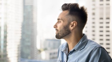 Hayalperest genç Latin adam şehir manzarasına bakıyor, gökdelen balkonundan manzaranın tadını çıkarıyor, şehir havasını kapalı gözlerle soluyor, gayrimenkulleri düşünüyor, gülümsüyor, sakin, rahat, kaygısız.