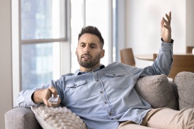 Sinirli genç Latin adam televizyon kumandası kullanıyor. Sinirli, sinirli, endişeli, futbol maçı seyrediyor.