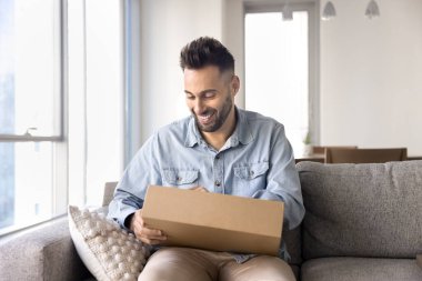 Neşeli Latin müşteri paketini açtı, evdeki kanepenin üzerindeki karton kutuyu açtı, paketin içinde internet mağazasından alınmasını bekledi, gülümsedi, güldü.