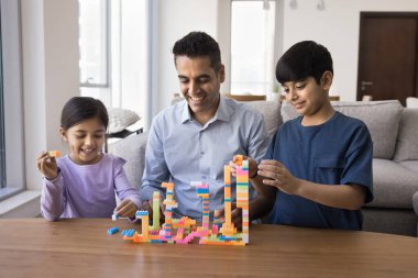 Mutlu Hintli baba, küçük kız ve küçük oğlan çocuklarıyla inşaat oyunu oynuyor. Baba ve çocuklar evlerinde renkli kuleler inşa ediyorlar, akıllı gelişim aktivitelerinin keyfini çıkarıyorlar.
