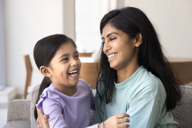 Neşeli genç Hintli anne sevimli kızına sarılıyor, duygusal olarak gülüyor, kucağına çocuk alıyor, sarılıyor, eğleniyor, annelikten keyif alıyor, eğlenceli aile eğlenceleri yapıyor.