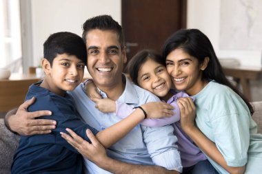 Mutlu, çekici Hintli bir aile çifti. İki küçük çocuğa sıcak bir kanepede sarılıyorlar. Mükemmel bir gülümsemeyle kameraya bakıp yakınlığın, rahatlığın ve poz vermenin tadını çıkarıyorlar.