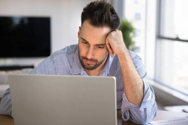 Düşünceli, Latin serbest girişimci adam dizüstü bilgisayarla ilgili çözümler düşünüyor, kafa sızdırıyor, ekranda metin okuyor, evdeki internet projesinde çalışıyor.