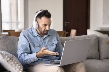 Gergin, kulaklıklı, evde dizüstü bilgisayara bakan, yazılımla ilgili sorunları olan, iş başvurusu yapan, web servisinde yanlış iş yapan, stresli ve hayal kırıklığına uğramış Latin serbest çalışan adam.
