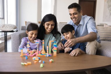 Mutlu Hintli anne ve baba çocuklara oyuncak kuleler yapmalarında yardım ediyor, renkli parçalar inşa ediyor, aile eğlencesinin tadını çıkarıyor, birlikte vakit geçiriyor, gülüyor, eğleniyor. Evde oynayan kardeş çocuklar ve ebeveynler