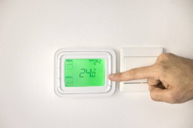 Erkek elinin termostatı düzenlemesini kapat, dairede hava sıcaklığı. Evdeki klima kontrol panelini kullanan adam, duvardaki düğmeye basarak ekranı, ekranı...