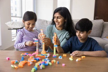 Genç Hintli anne ve iki çocuğun birlikte inşaat oyunu oynamaları oyuncak şehri istiflemeleri renkli yapı taşlarından kuleler inşa etmeleri gülümsemeleri, gülmeleri, aile zamanlarını evde geçirmeleri.