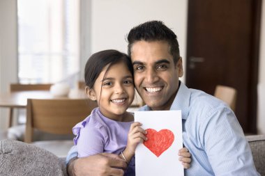 Mutlu Hintli baba-kız portresi. Kırmızı kalple el çizilmiş tebrik kartı. Kameraya bakıyor, kanepede oturuyor ve sarılıyor, babalar gününden zevk alıyor.